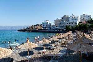 ein Strand mit vielen Sonnenschirmen und Menschen im Wasser in der Unterkunft Beachfront Salty Sea Luxury Suite 1 in Agios Nikolaos