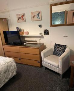 um quarto com uma cómoda, uma televisão e uma cadeira em EsJays at Knowles House em Lytham St Annes