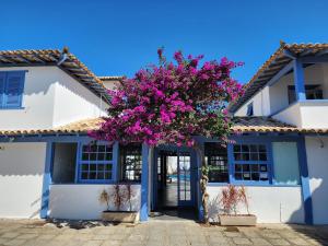 a white building with a tree with pink flowers at Pousada Vila Capri in Búzios