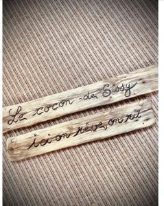 dos piezas de madera con escritura en una cama en Le cocon de sissy en Saintes-Maries-de-la-Mer
