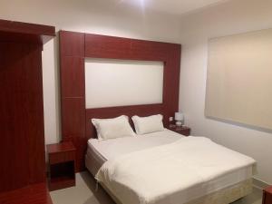 a bedroom with a white bed with a wooden headboard at مراسم رفحاء للشقق المخدومة in Rafha