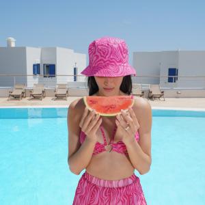 una mujer con un sombrero rosa sosteniendo una porción de sandía en El Sol Hotel en Kapsálion
