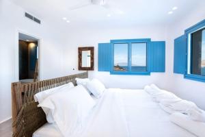 Schlafzimmer mit einem großen Bett mit weißer Bettwäsche und blauen Fenstern in der Unterkunft Myko Grand Villa by Bestofmikonos in Ftelia
