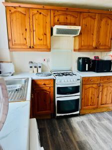 uma cozinha com um fogão, um lavatório e armários de madeira em Quiet Single bedroom with free parking, office desk &chair, free wifi em Harrowden