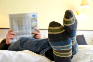 une personne portant des chaussettes rayées qui lit un livre sur un lit dans l'établissement Arnimsruh Hotel garni, à Lübeck