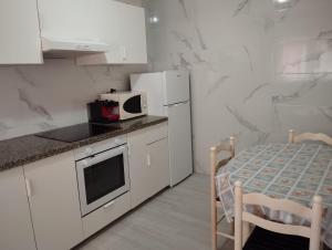 a white kitchen with a table and a microwave at Apartamento céntrico Prado Blanco in Finisterre