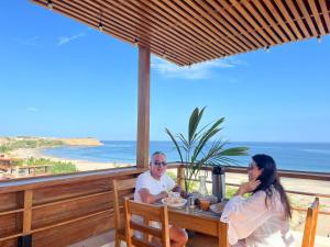 two people sitting at a table with a view of the beach at PUNTA VELEROS ROOFTOP in Los Órganos