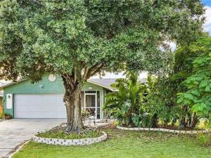 a house with a tree in front of a driveway at 7 Palms Pool House in Cape Coral