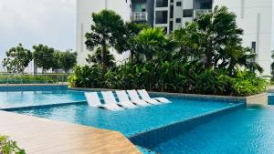 una piscina con tumbonas blancas en un edificio en Sunway lagoon Greenfield 3R2B w/tvbox, en Petaling Jaya