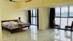 Un niño sentado en una cama en una habitación con ventanas en Manu's Home Stay, en Malayāttūr