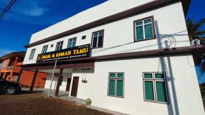 un bâtiment blanc avec un panneau indiquant de tourner un groupe de musique dans l'établissement Bilik & Rumah Tamu Ketereh, à Ketereh