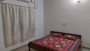 a bedroom with a bed with a red blanket and a window at Suburbs Holiday Home in Dabolim