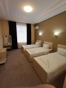 タシュケントにあるGRAND KARAVAN HOTELのベッド3台とテレビが備わるホテルルームです。