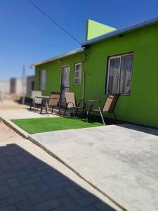 ein grünes Gebäude mit Stühlen und einem Tisch davor in der Unterkunft Kangumine Self Catering Units in Okakarara