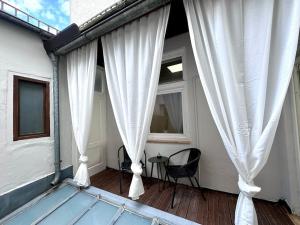 eine Veranda mit weißen Vorhängen sowie einem Tisch und Stühlen in der Unterkunft LendLoft: Altbaumodern & Lendviertel Chic in Klagenfurt am Wörthersee