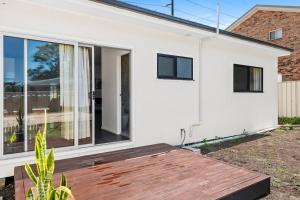 una casa blanca con una terraza de madera delante de ella en 4Bed Modern Oasis by Train Station, en Wyong