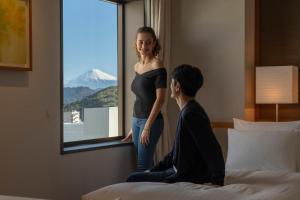 a woman standing in a hotel room looking out a window at Hotel Associa Shizuoka in Shizuoka