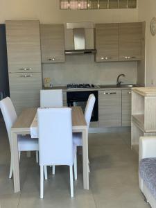 uma cozinha com uma mesa de madeira e cadeiras brancas em Villetta a Schiera - Bosa Marina em Magomadas