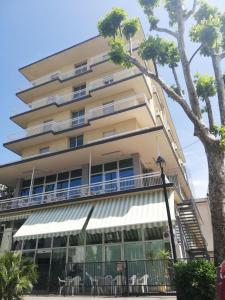 een hoog gebouw met tafels en stoelen ervoor bij Hotel Concordia Palace in Rimini