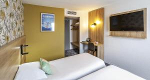 a room with two beds and a flat screen tv at Ostal Pau Universite - Sure Hotel Collection by Best Western in Pau