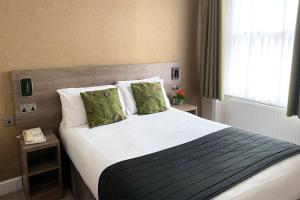 a bedroom with a large bed with white sheets and green pillows at Kensington Gardens Hotel in London