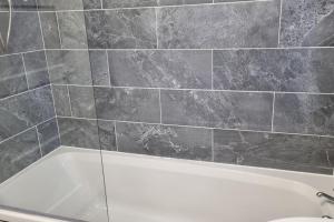 a bathroom with a white tub and a tile wall at The Lodge Manchester Airport Free parking Wi-Fi in Wythenshawe