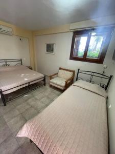 1 dormitorio con 2 camas, silla y ventana en Vasilikos Apartments, en Paralia Agias Foteinis