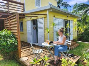 a woman sitting at a table in front of a tiny house at Le Petit Bungalow Créole in Saint-Pierre