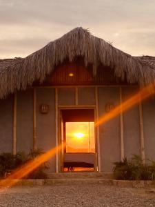 a house with a straw roof with the sunset in the window at La Cabaña de Iza in Canoas