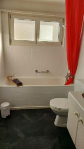 a bathroom with a tub and a toilet and a red curtain at Apartment Heidi in Spiez