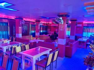 a restaurant with pink lighting and tables and chairs at HOTEL INDRAPRASTHA in Māldah