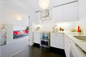 a white kitchen with white cabinets and a living room at Zone 1! 2 bed duplex Apartment! in London