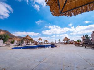 patio z ławkami i parasolami oraz basenem w obiekcie B&W SAHARA SKY CAMP w mieście Qasr Al Farafirah