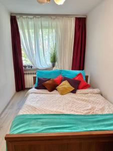 a bed with colorful pillows in front of a window at Sunny Apartment in Silesia in Czeladź