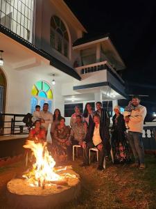um grupo de pessoas sentadas em torno de uma lareira em frente a uma casa em Hestia Chalet 3BHK Villa em Ooty