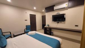 a room with a bed and two chairs and a tv at Hotel JANAS in Tirupati