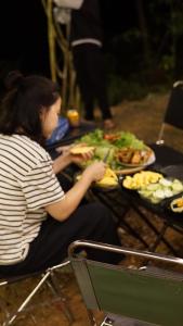 kobieta siedząca przy stole z talerzami jedzenia w obiekcie Konoha Măng Đen w mieście Kon Von Kla