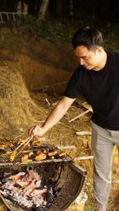 Mężczyzna gotuje jedzenie na grillu. w obiekcie Konoha Măng Đen w mieście Kon Von Kla