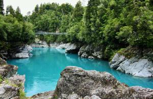 a blue river with a bridge in a forest at Prime Beachfront Retreat in Hokitika