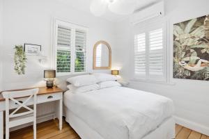 a white bedroom with a desk and a bed at Tranquil 2-Bed Family Home with Deck Among Trees in Brisbane