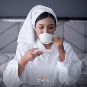 a woman in a robe drinking from a coffee cup at Stonehill Suites in Bacolod