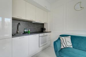 a kitchen with white cabinets and a blue couch at Sunny Garden by Grand Apartments in Gdańsk