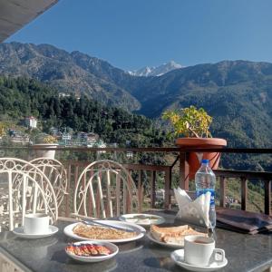 a table with plates of food on a balcony with mountains at Holiday Hill, Mcleodganj, Dharamsala in Dharamshala