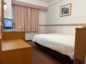 新潟市にあるホテルアルファーワン新潟のベッド、デスク、コンピュータが備わるホテルルームです。