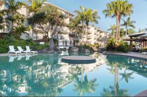 uma piscina num resort com palmeiras e edifícios em Ocean View - Alexandra Headlands Beachfront Unit em Alexandra Headland