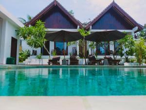 a villa with a swimming pool with chairs and umbrellas at The Local Are Guling in Kuta Lombok