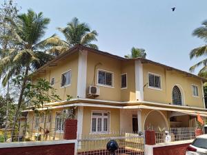 a yellow house with palm trees in the background at OYO Shooolin Homestay in Goa