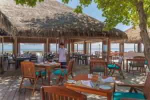 拉斯杜環礁的住宿－Veligandu Maldives Resort Island，站在餐厅前的男人,有桌椅