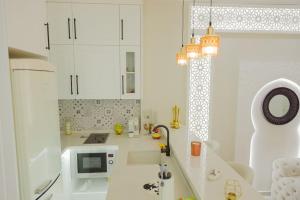 eine weiße Küche mit einer Spüle und einer Mikrowelle in der Unterkunft Maison SOUAD in Mahdia