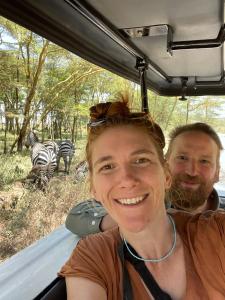 Ein Mann und eine Frau in einem Fahrzeug mit Zebras im Hintergrund. in der Unterkunft Homebase gardens in Nakuru